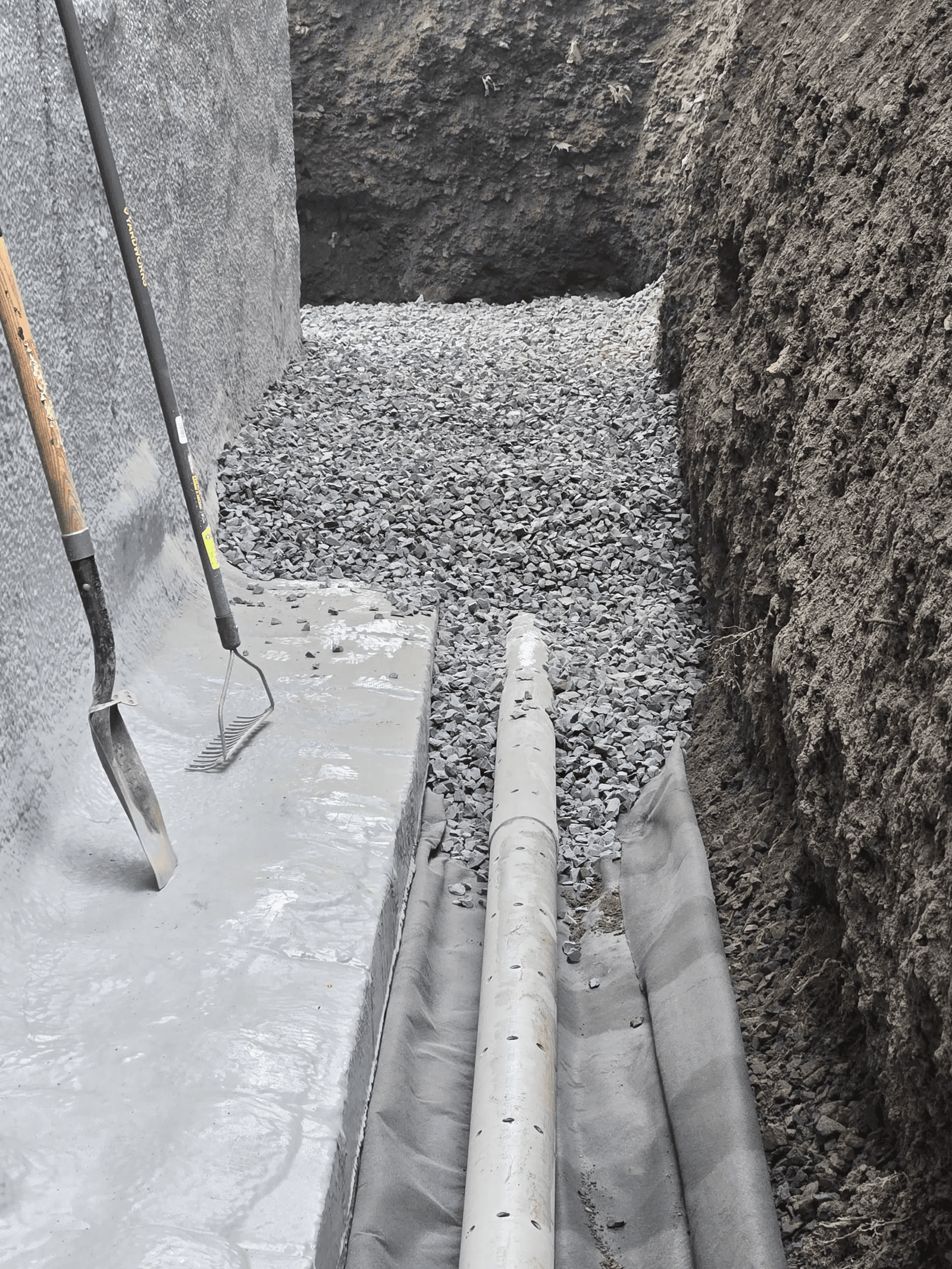 Close-up of a French drain being installed with geotextile membrane and gravel along a foundation