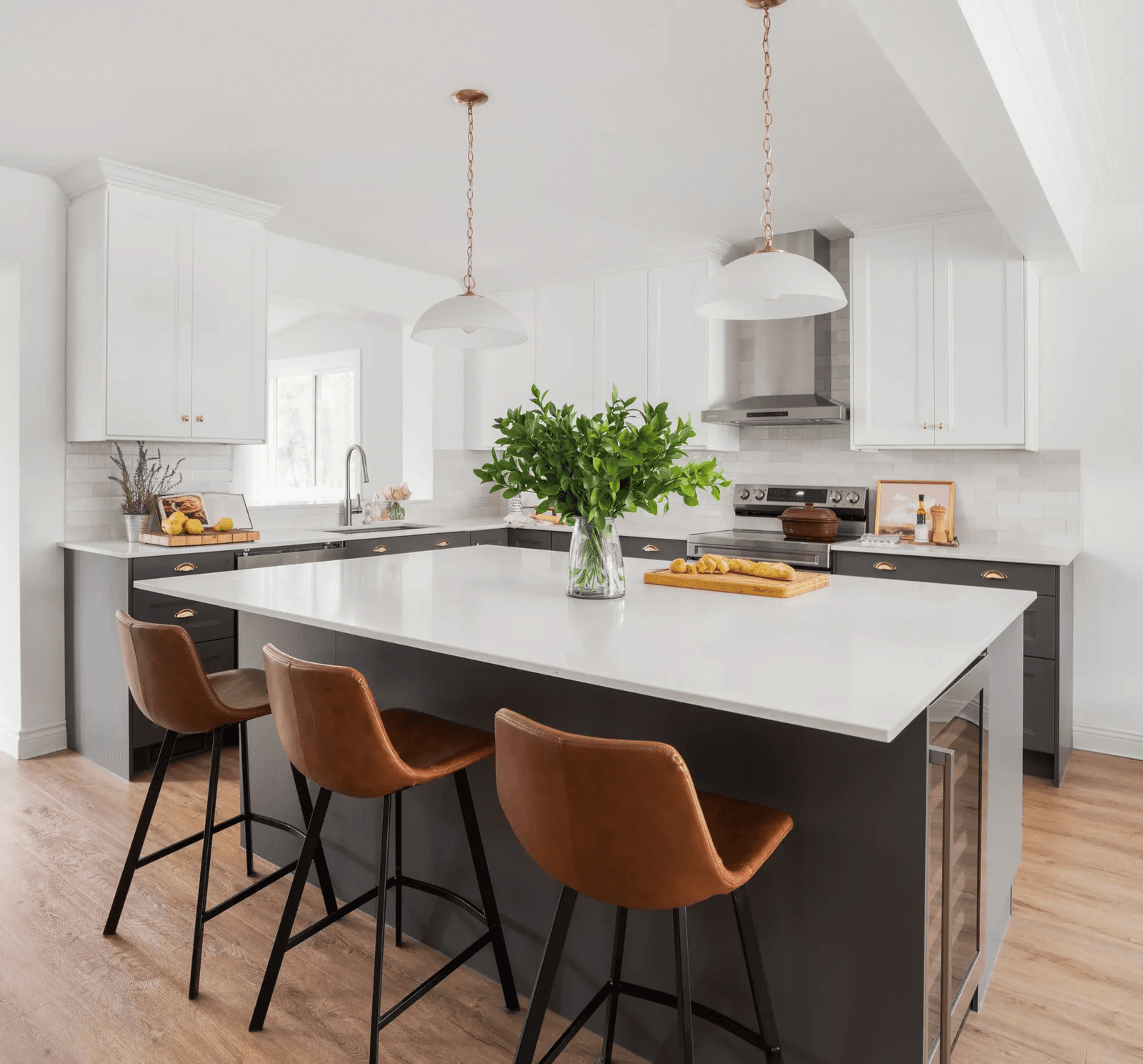 Transitional-style kitchen in Montreal featuring a matte black central island with a white quartz countertop. White Shaker cabinets and copper handles add elegance, while light wood flooring and brown leather stools create a warm and inviting atmosphere.