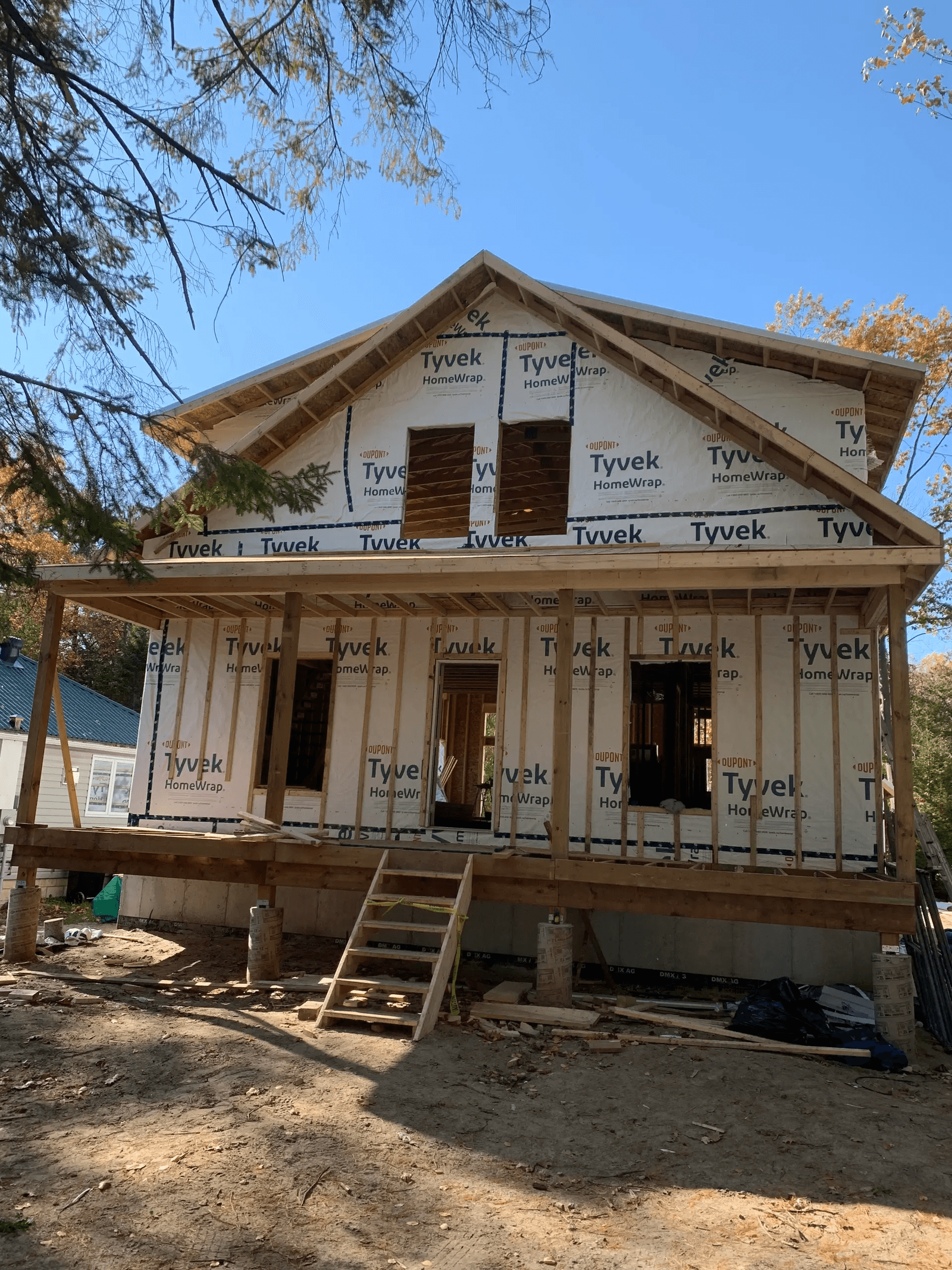 House under construction with a wooden framework and building wrap at a residential site.