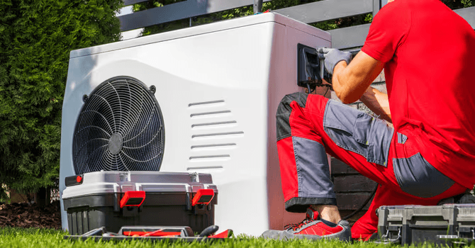 HVAC technician servicing or repairing an outdoor heat pump unit with maintenance tools nearby.