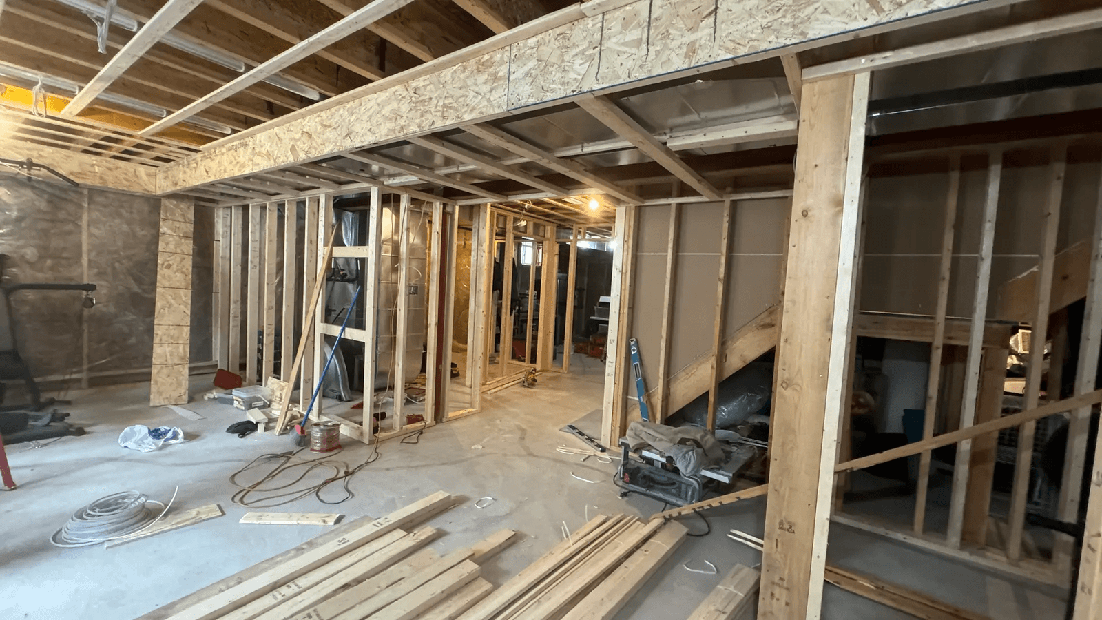 Basement under renovation with wooden framing, electrical wiring, and ongoing finishing work.