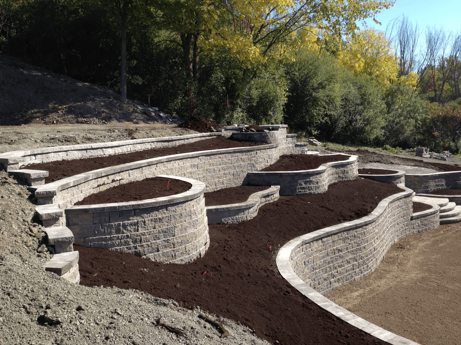 Terraced landscaping with multiple curved concrete block retaining walls, integrated steps and planting areas on a sloped property