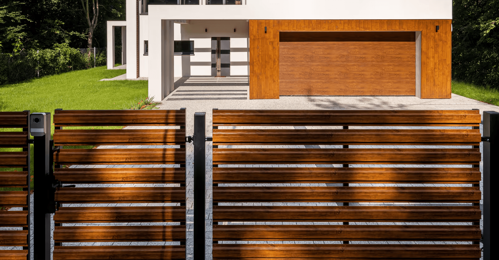Modern horizontal aluminum slat driveway gate with black metal posts and an access control system, in front of a contemporary house with a matching wood-finish garage door.
