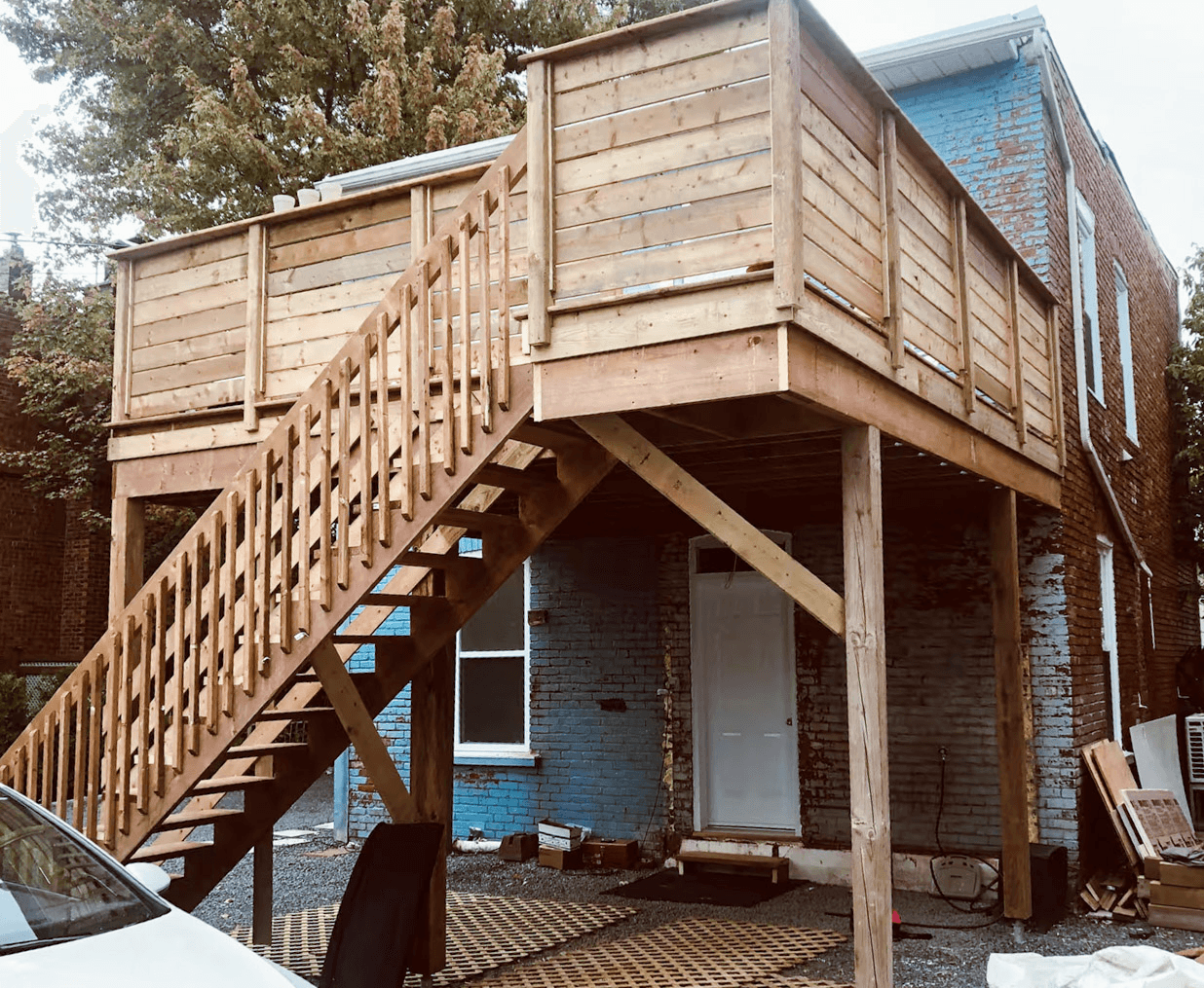 Raised wood deck with stairs, railing, and supporting structure attached to a brick house