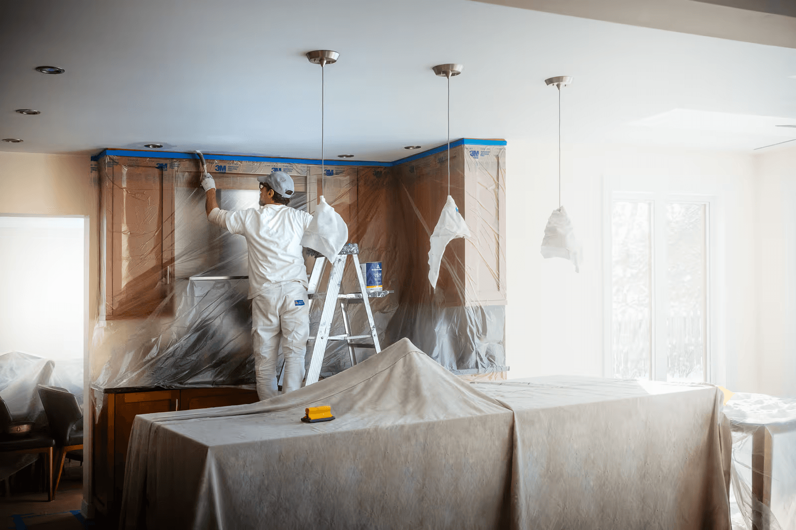 Professional painter preparing and painting a residential kitchen with cabinets masked in plastic and surfaces protected during the work