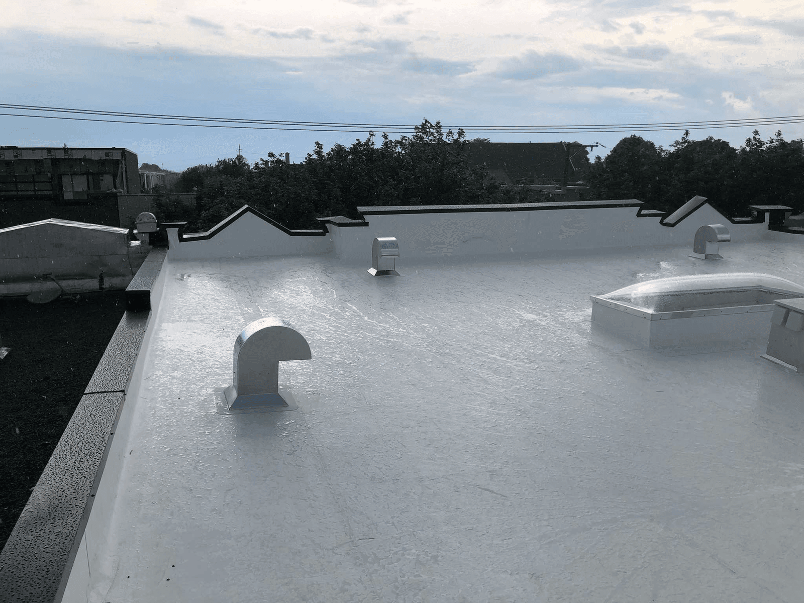 White flat roof with waterproof coating, ventilation openings, and a skylight under the rain.