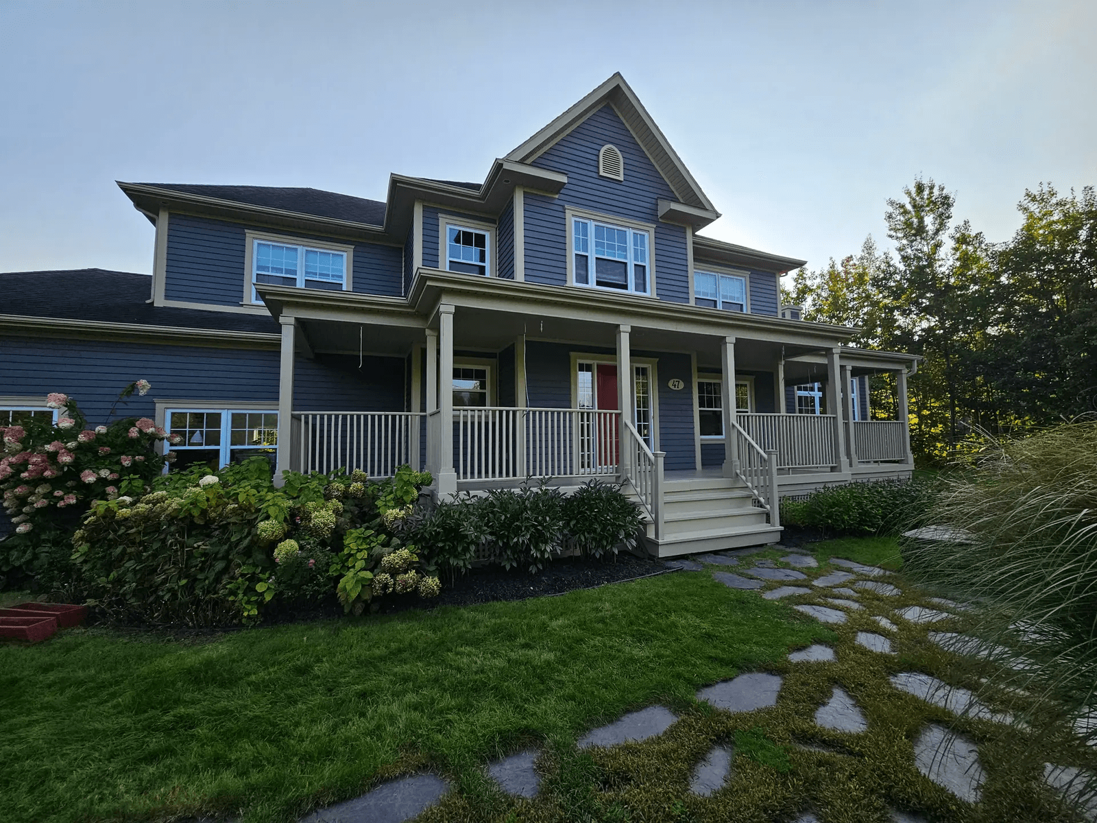 Two-story blue house with front porch and flowered landscaping