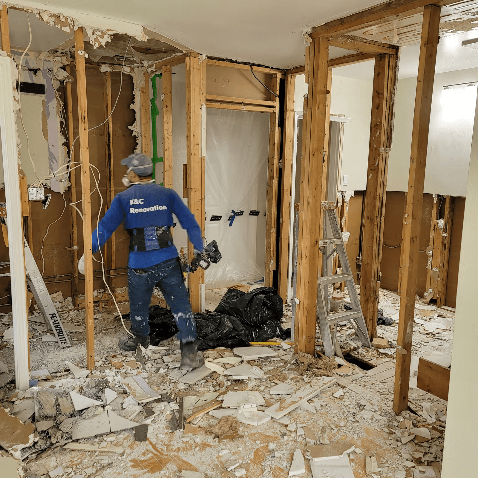 Interior demolition work with exposed wall framing and a renovation contractor removing construction debris.