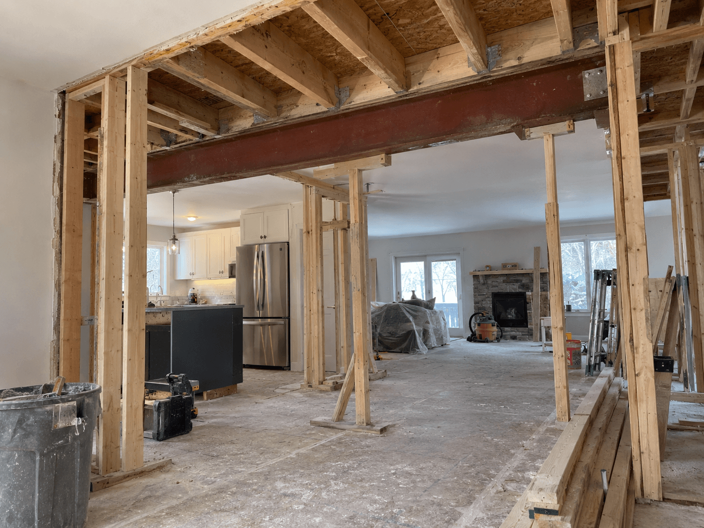 Home undergoing interior renovation with a large structural opening reinforced by a steel beam, exposed wood framing and temporary support posts
