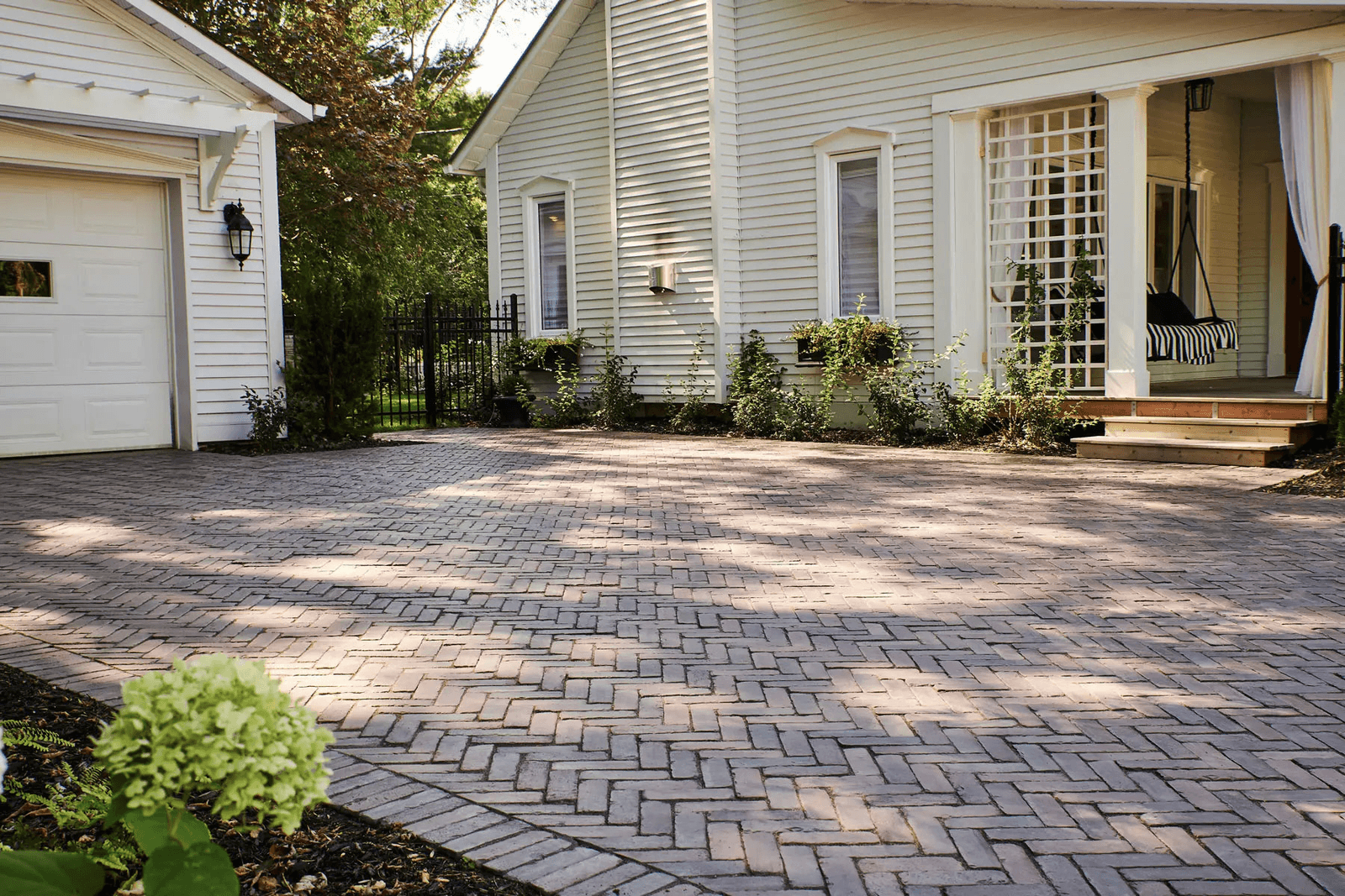 Brick-style interlocking stone driveway with landscaping in front of a white house.