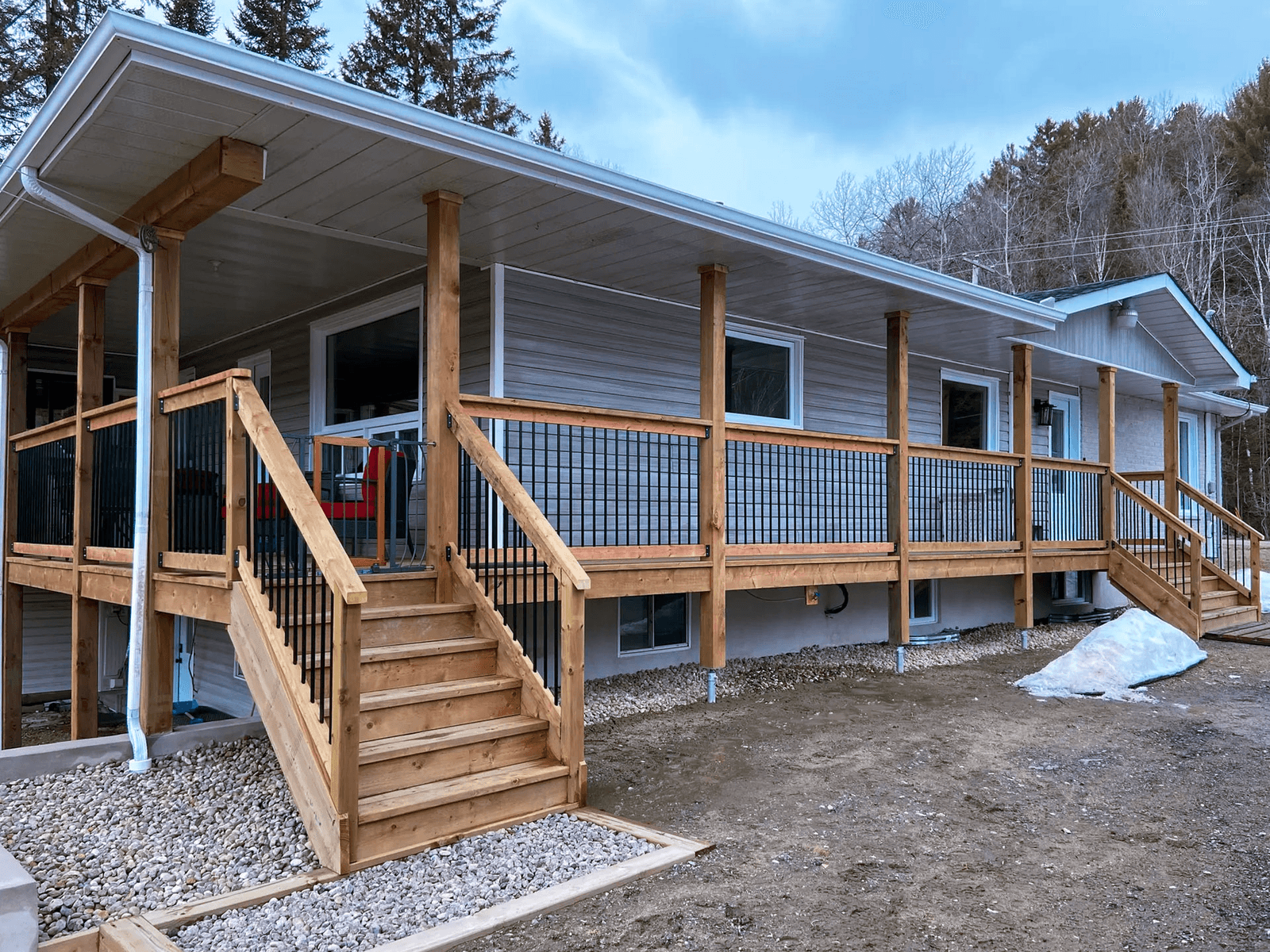 Large raised wood deck with stairs, black railings, and support posts in front of a residential home