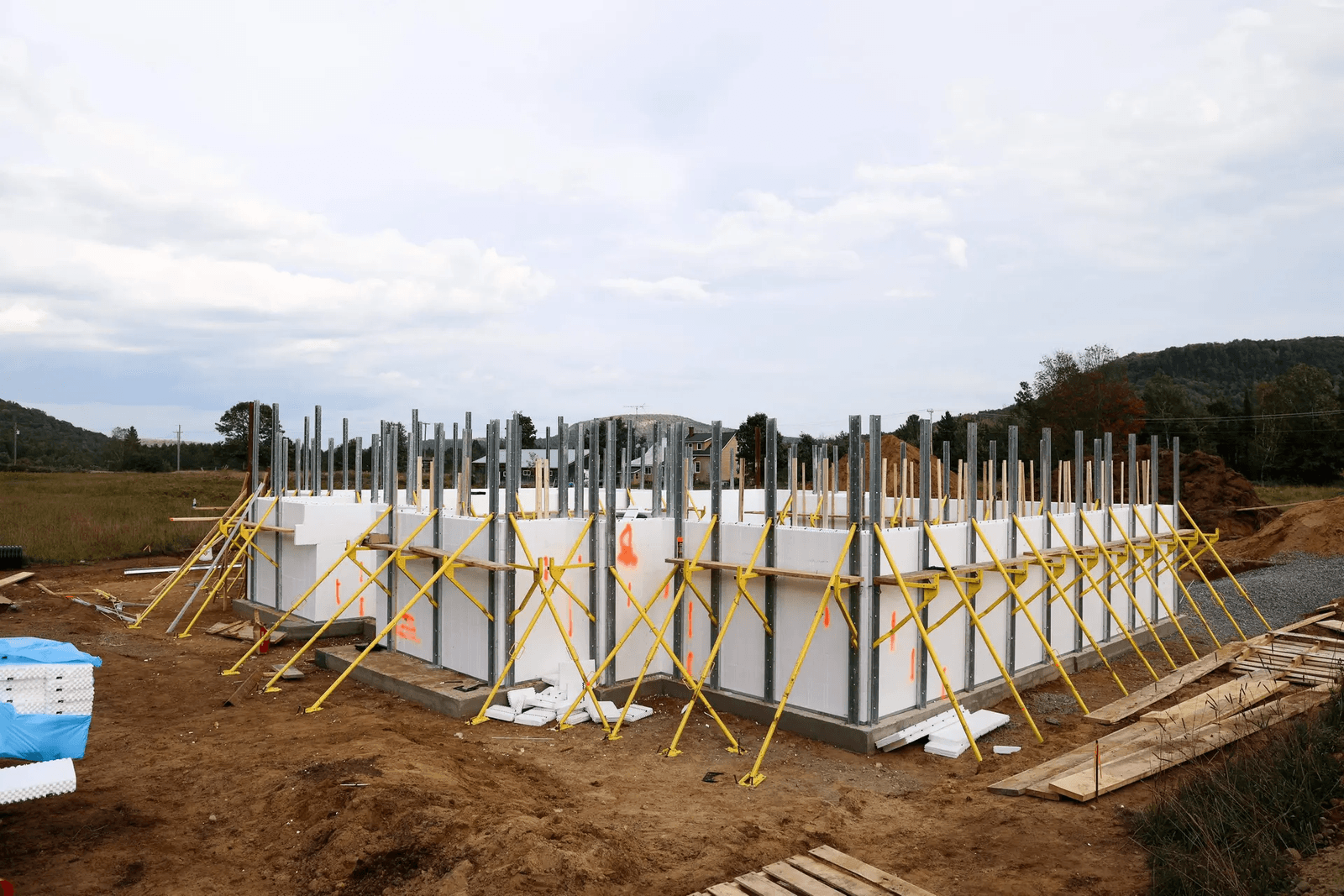 Residential foundation under construction with insulated concrete forms, modular panels, metal supports, bracing, and structural preparation for a new home