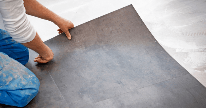 Installer laying a gray floor tile on a prepared adhesive surface during interior renovation work.
