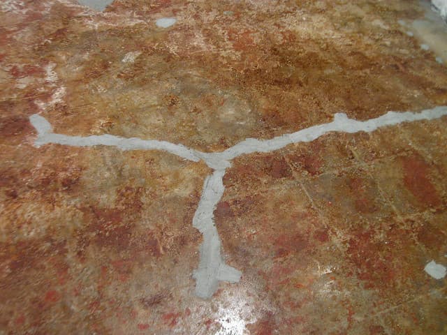 An interior floor showing several visible cracks that have been filled or repaired, with a worn and stained surface.