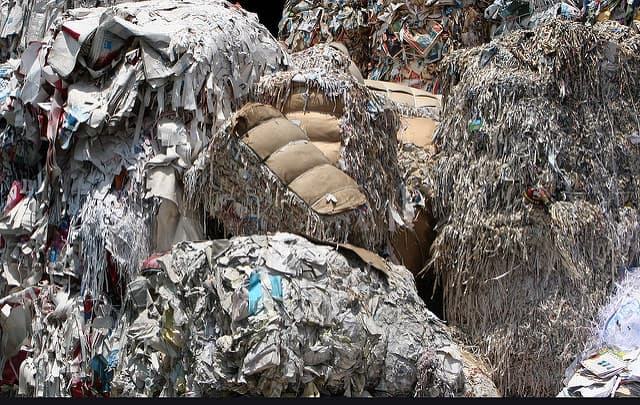 Bales of recycled paper and cardboard stacked in a recycling facility, used as raw material for cellulose insulation.