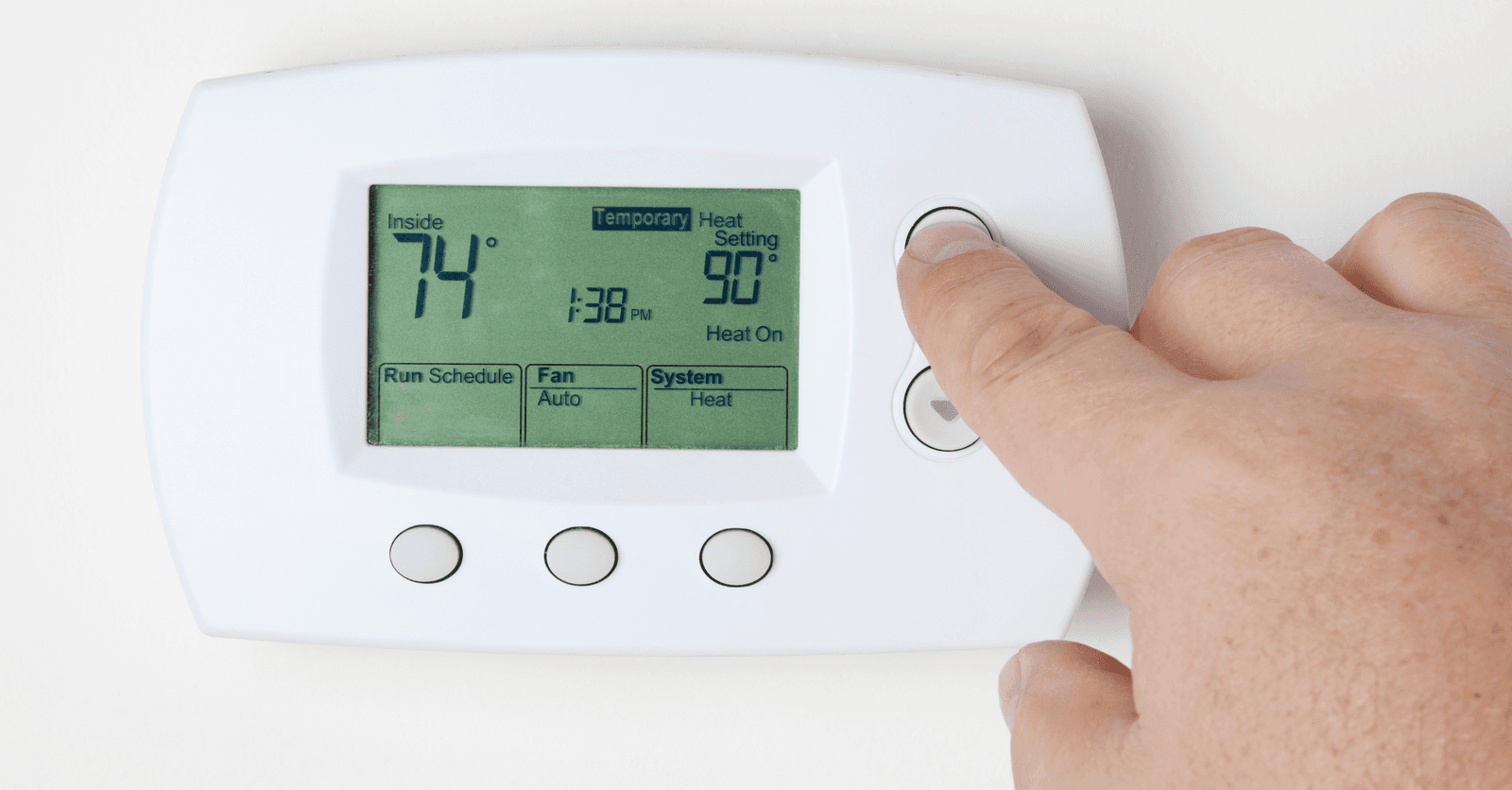 Hand adjusting a digital thermostat to regulate indoor temperature.